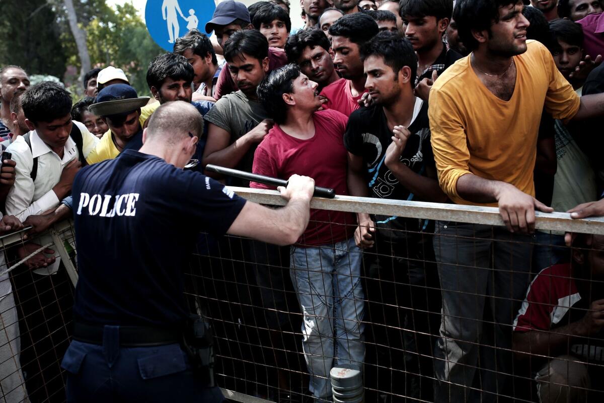 A Greek police officer tries to push back migrants waiting to be registered on the island of Kos on Monday. The number of migrants and refugees arriving on Greece's shores has exploded this year, with the nearly 50,000 who entered in July surpassing all of 2014.