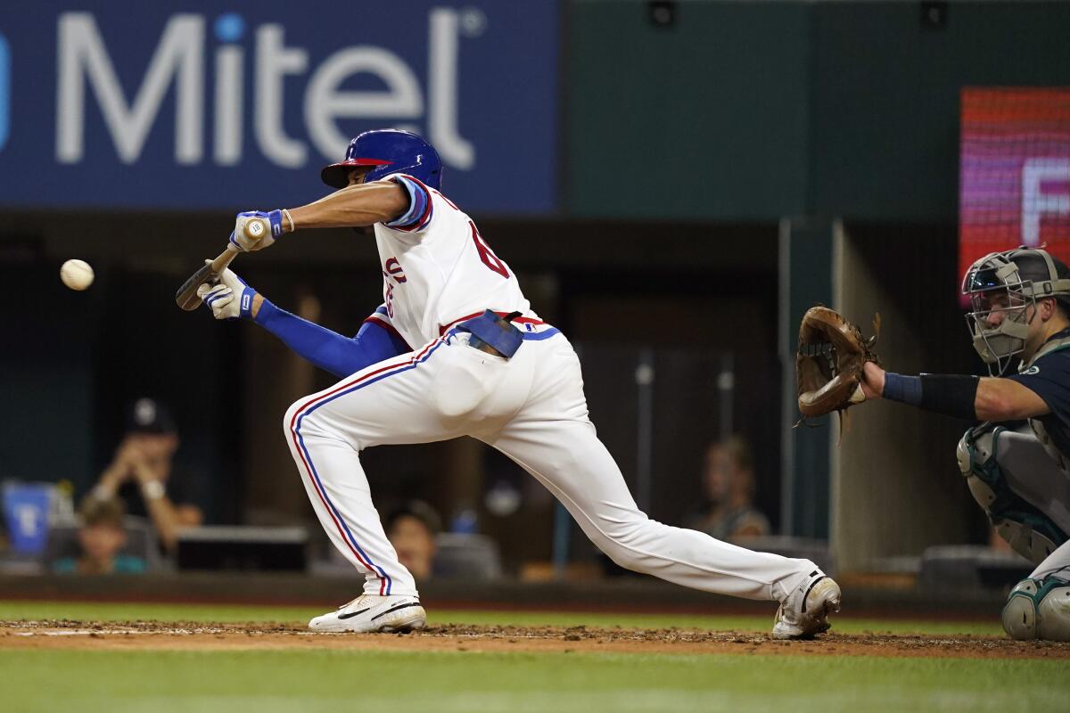 Texas Rangers' Bubba Thompson, left, hits a sacrifice bunt in front of Seattle Mariners catcher Cal Raleigh during the fourth inning of a baseball game in Arlington, Texas, Saturday, Aug. 13, 2022. Rangers' Charlie Culberson scored on the play. (AP Photo/LM Otero)