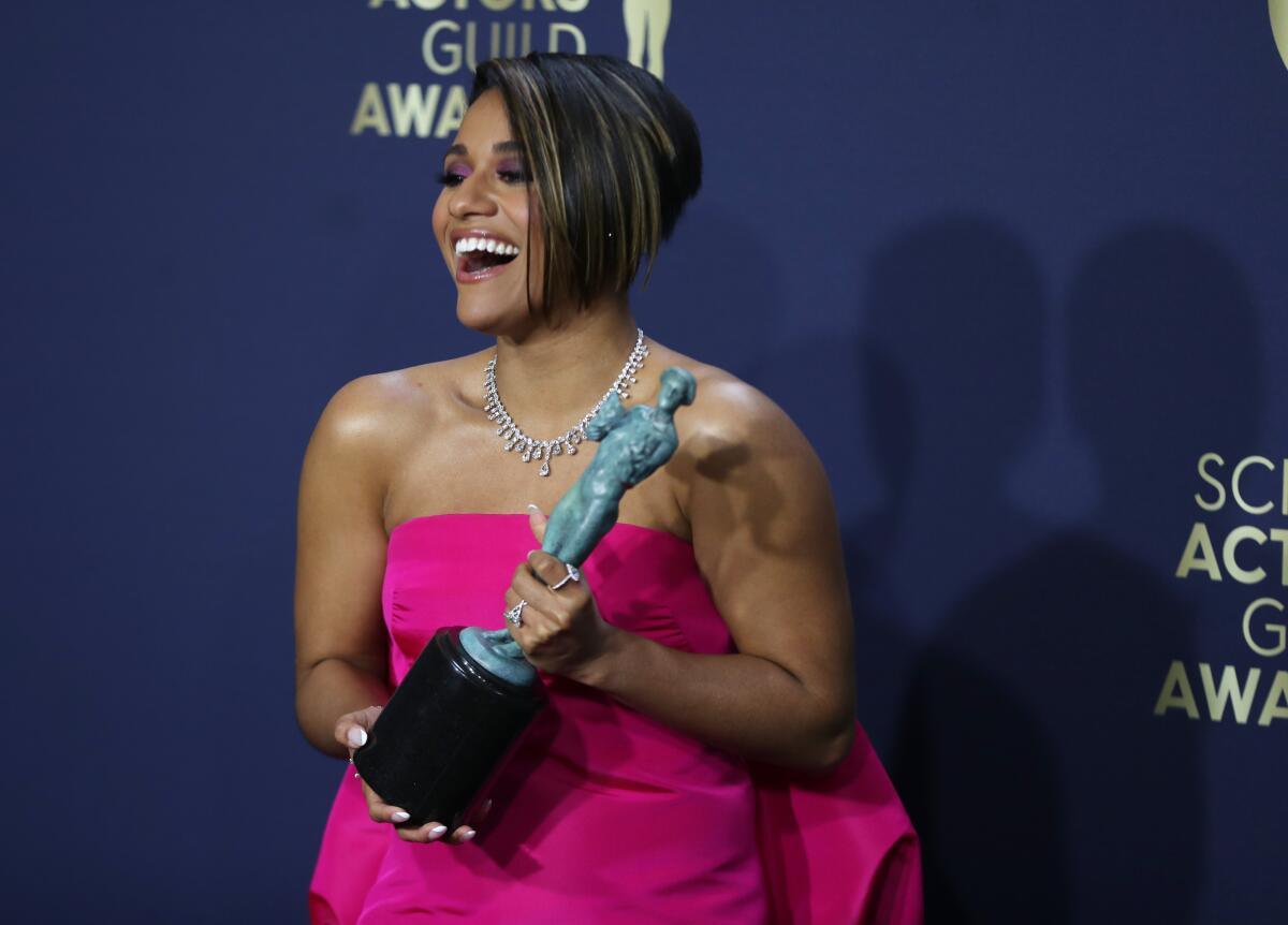 A smiling woman in a bright fuschia gown holds a trophy. 