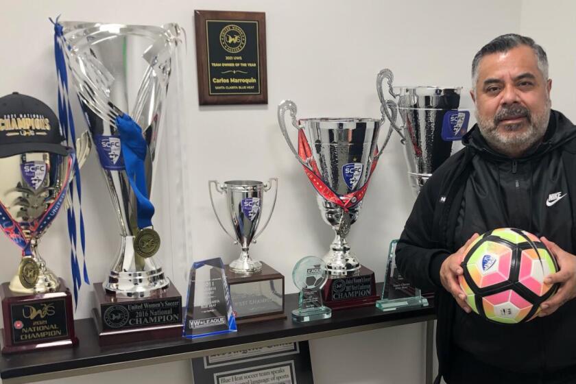 Carlos Marroquin stands next to trophies and awards won by the Santa Clarita Blue Heat.