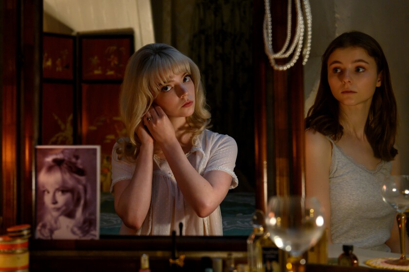 Reflected in a mirror, Anya Taylor-Joy, left, puts on earrings standing next to Thomasin McKenzie in "Last Night in Soho."
