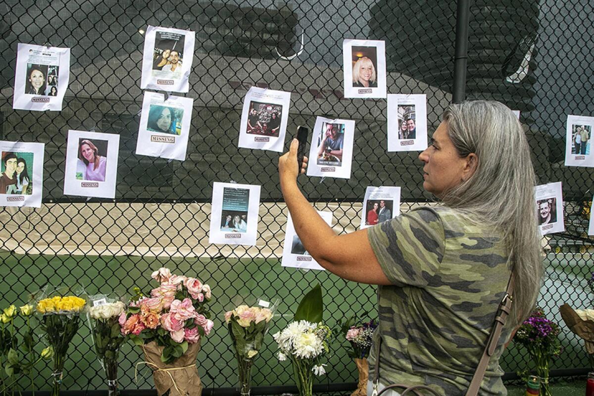 Photos of missing people are posted on a fence near a collapsed condo tower in Surfside, Fla.