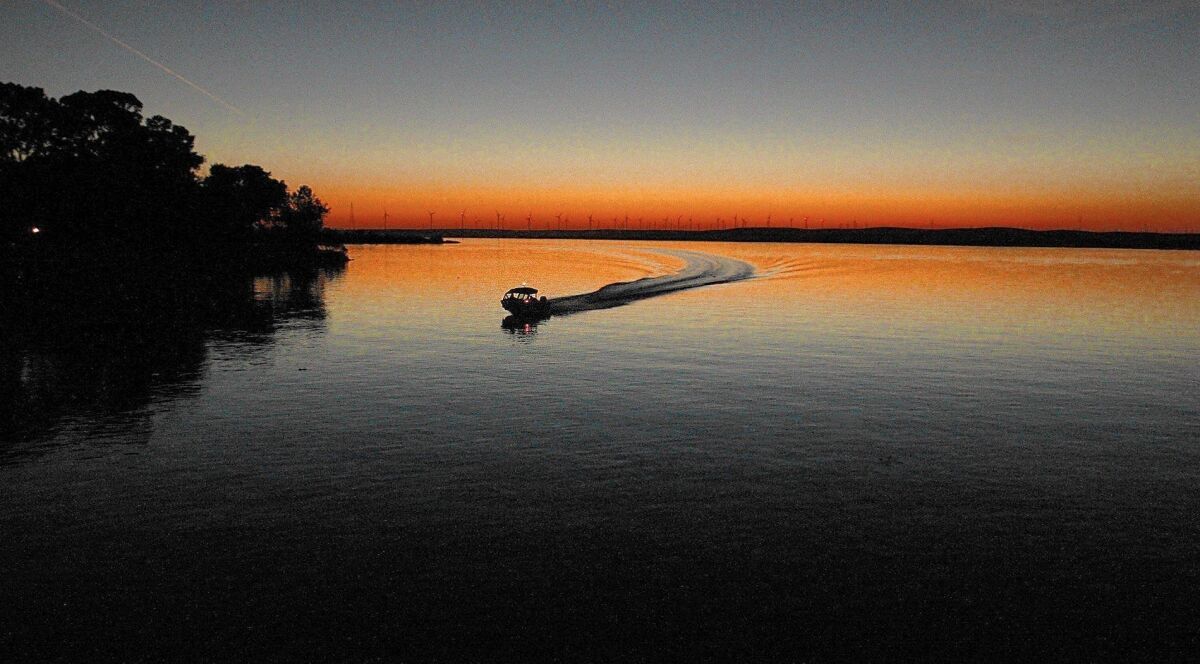 A boat traveling on a large body of water as the sun sets 