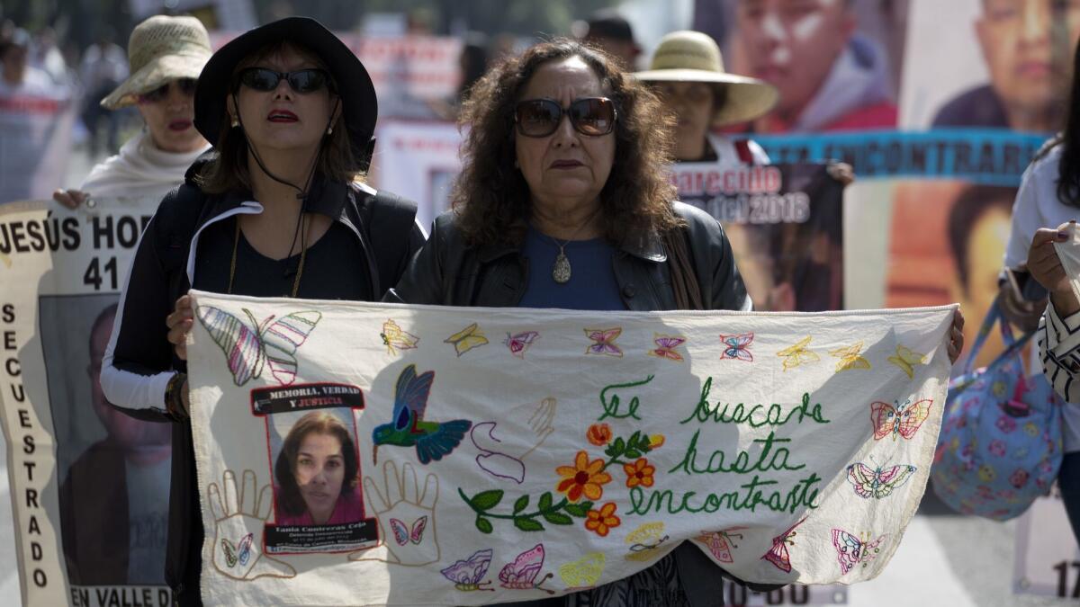 A woman holds a blanket embroidered with the message "I will look for you until I find you" and adorned with an image of a disappeared youth during a march in Mexico City on May 10, 2018, which is Mother's Day in Mexico.