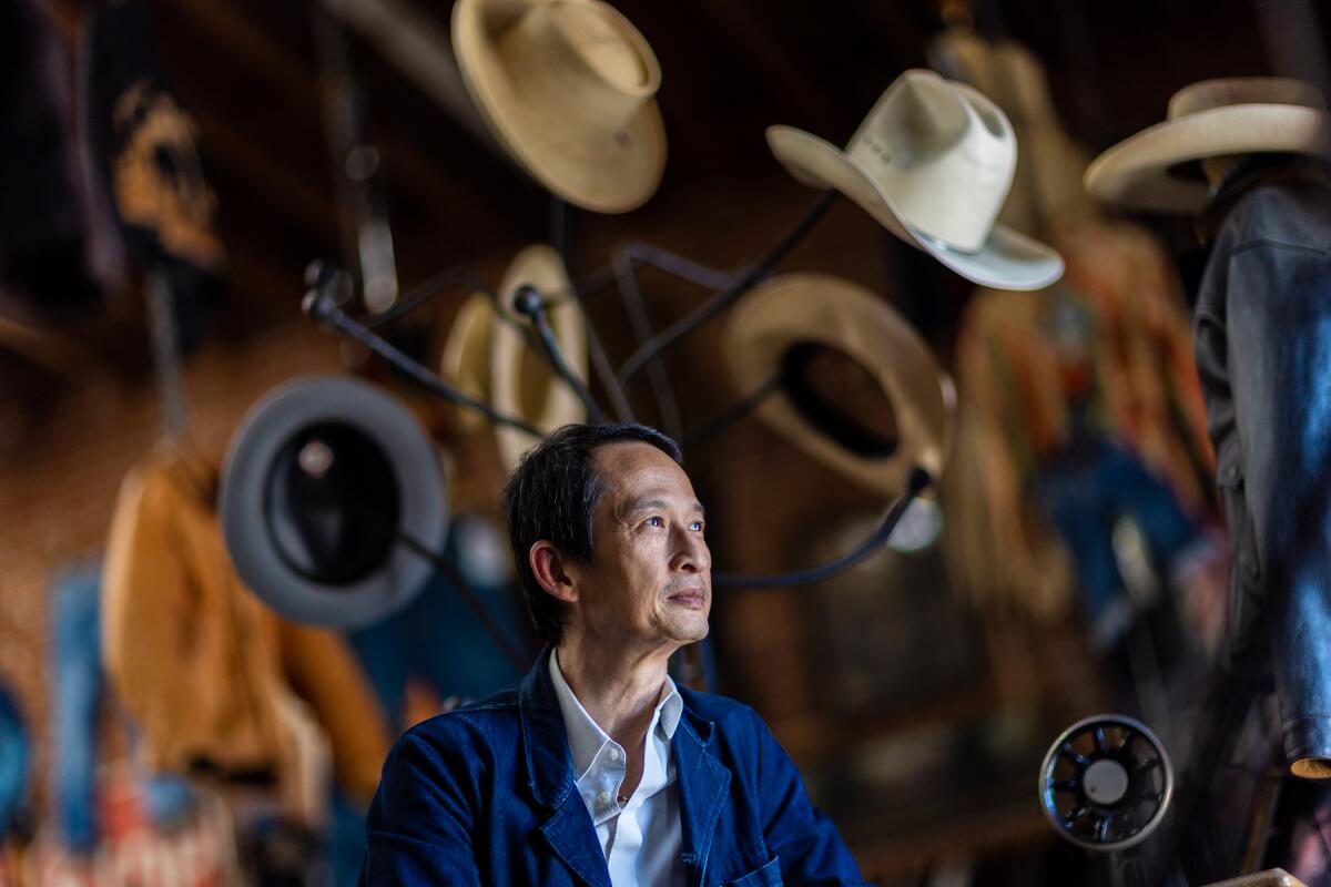 Tran Anh Hung sits in front of a hat rack.