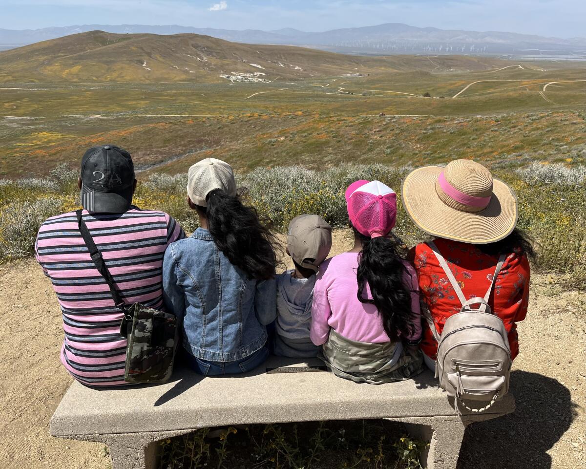 A family sits on a bench looking out over hills and mountains in the distance.