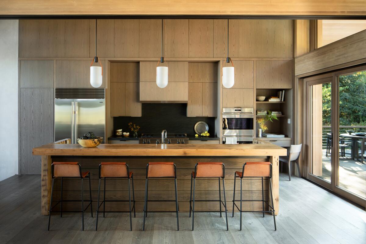 Pendant lights hover over a dining nook in a kitchen, inspired by the blackened metal and tan leather of the counter stools.