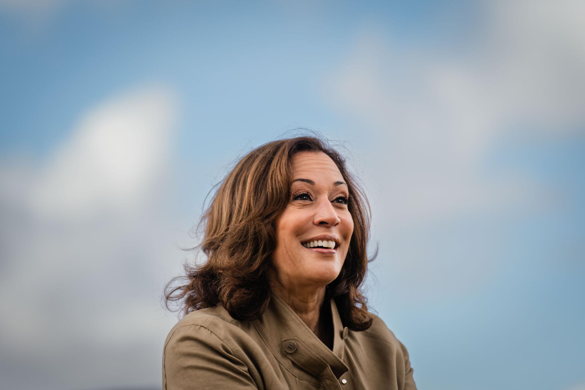 A head-and-shoulders frame of Kamala Harris against a soft blue sky with clouds.