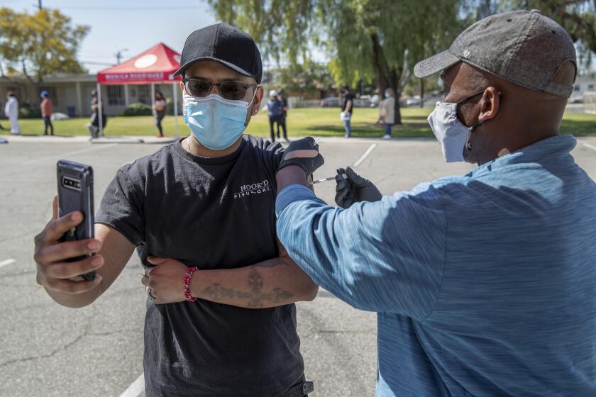 PACOIMA, CA - MARCH 04, 2021:Sergio Martinez, 32, left, of Mission Hills, takes video of himself receiving a vaccine shot from physician's assistant Jerry Brown at a COVID-19 vaccination pop-up site located at Valley Crossroads Seventh Day Adventist Church in Pacoima. Martinez owns a restaurant in Northridge called Hook'd Fish Grill. COVID-19 vaccination pop-up sites are being offered to residents of Los Angeles City Councilwoman Monica Rodriguez's district in the Northeast San Fernando Valley over the next three weeks. (Mel Melcon / Los Angeles Times)