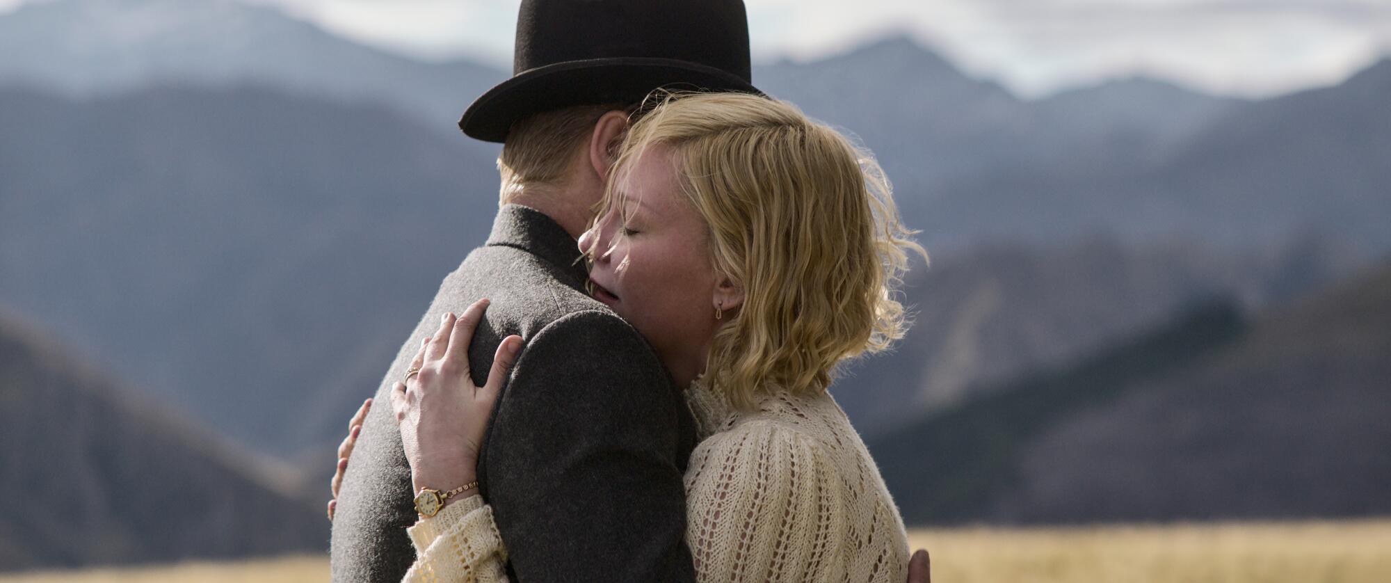 A man and woman hug in front of a backdrop of mountains.