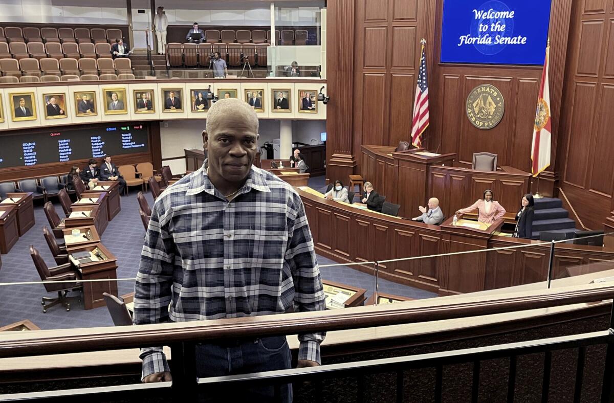 A man standing in the gallery above the floor of a legislative chamber, where a sign reads, "Welcome to the Florida Senate."