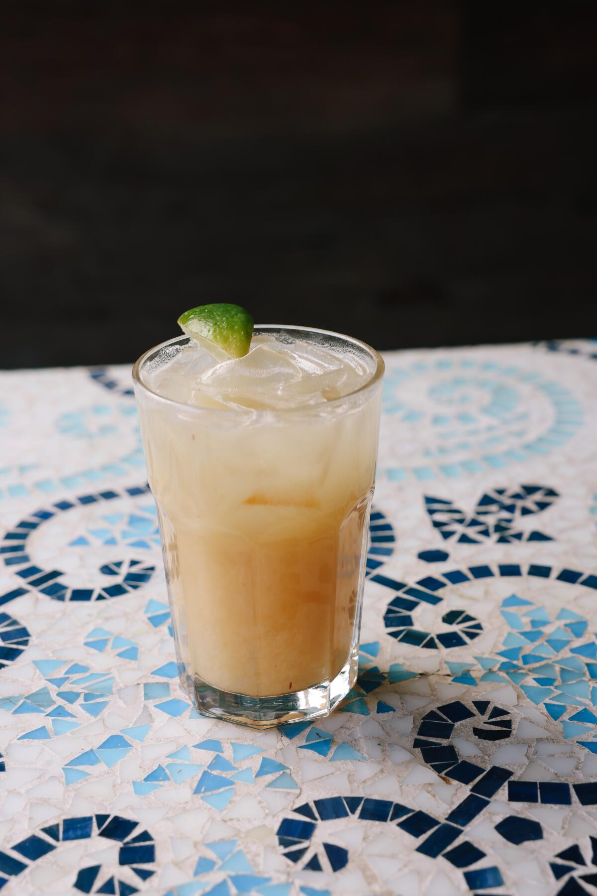 An iced coco-piña-guava fresca drink, garnished with a lime, on a mosaic-patterned surface