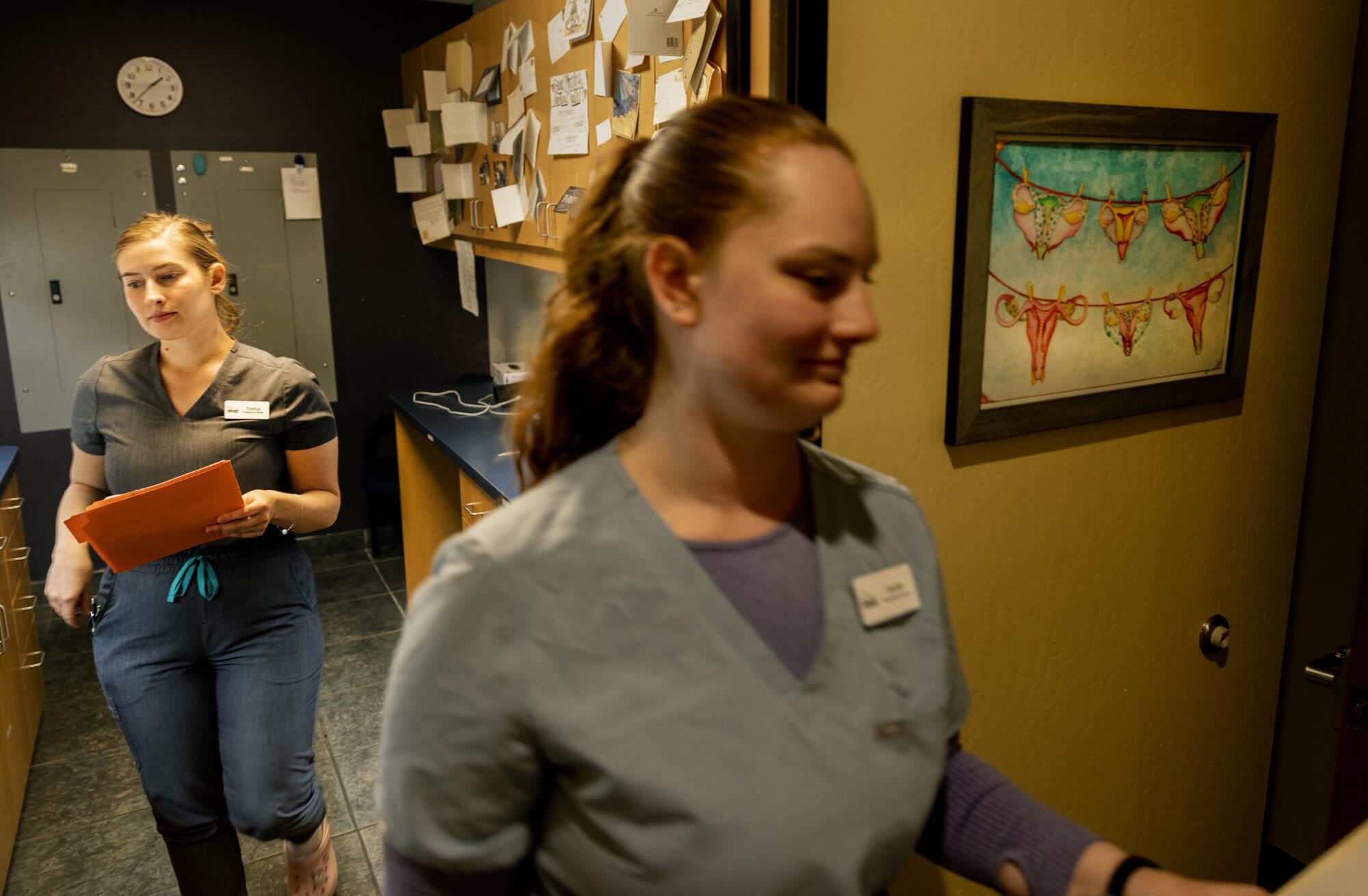 Nurses carry charts to exam rooms past thank you cards tacked to cupboards and artwork of a uterus hanging on a clothesline. 