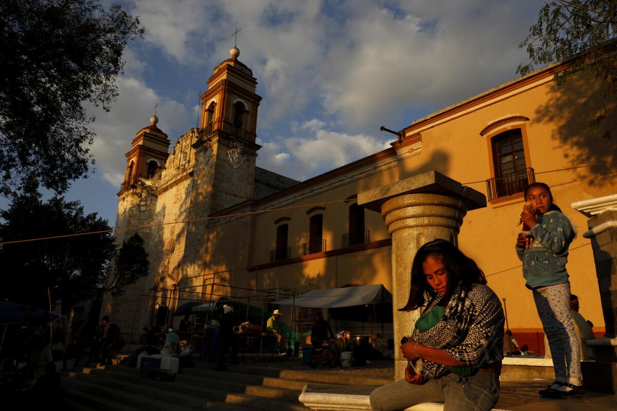 A young woman feeds her baby in front of Nuestra Señora de la Asuncion Catholic Church that anchors the Esplanada Benito Juarez. (Gary Coronado / Los Angeles Times) More Photos
