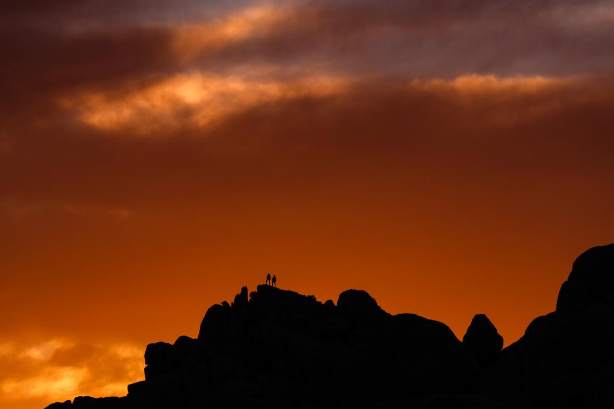 A glowing orange and red sunset over hikers atop rocks.