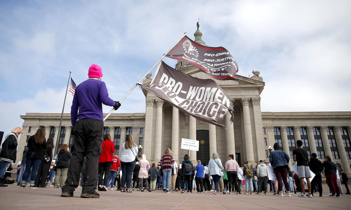 A person holds flags on the steps on Oklahoma state Capitol with a crowd of people