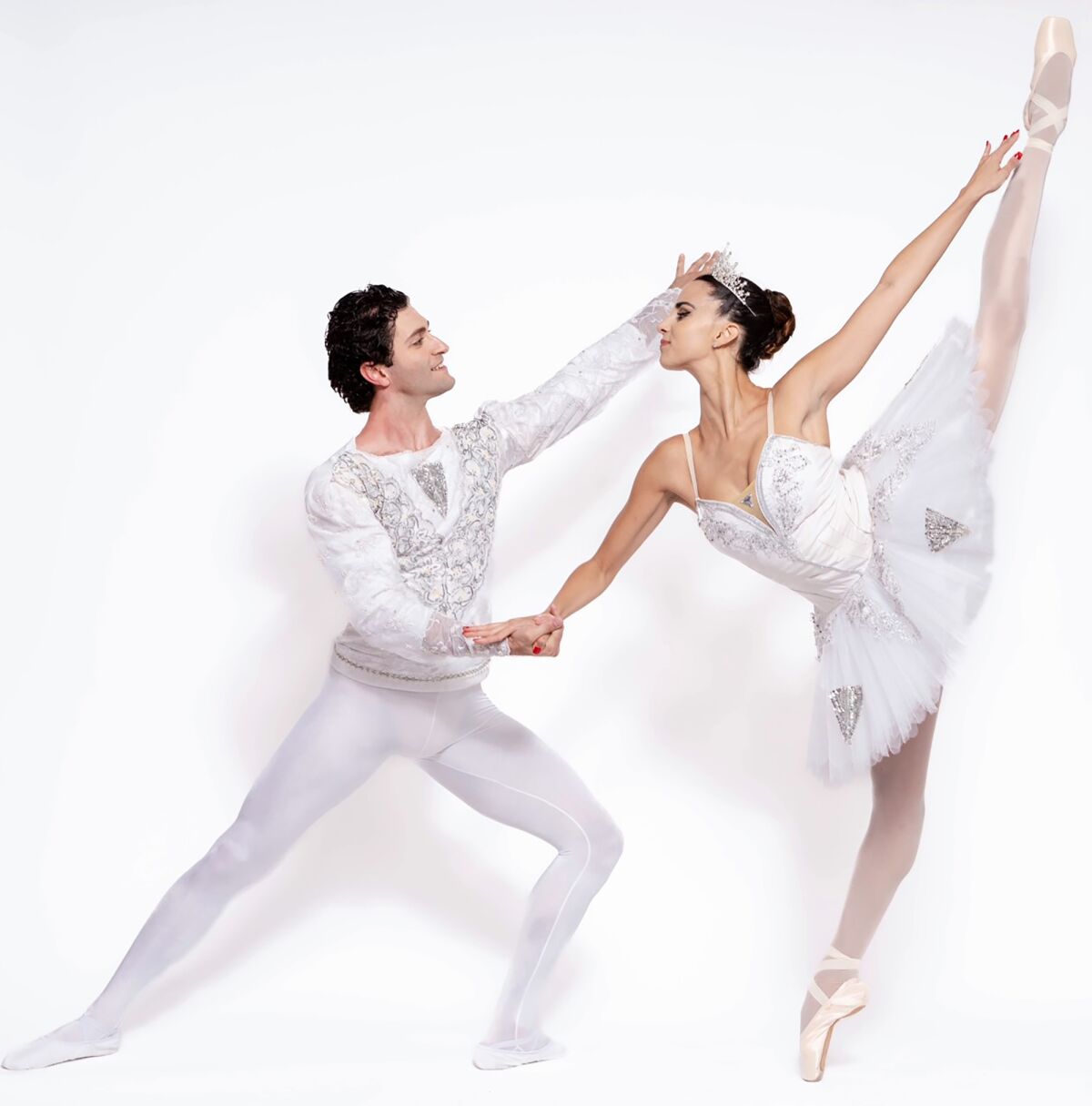 A male ballet dancer lunges, with a ballerina on pointe. 