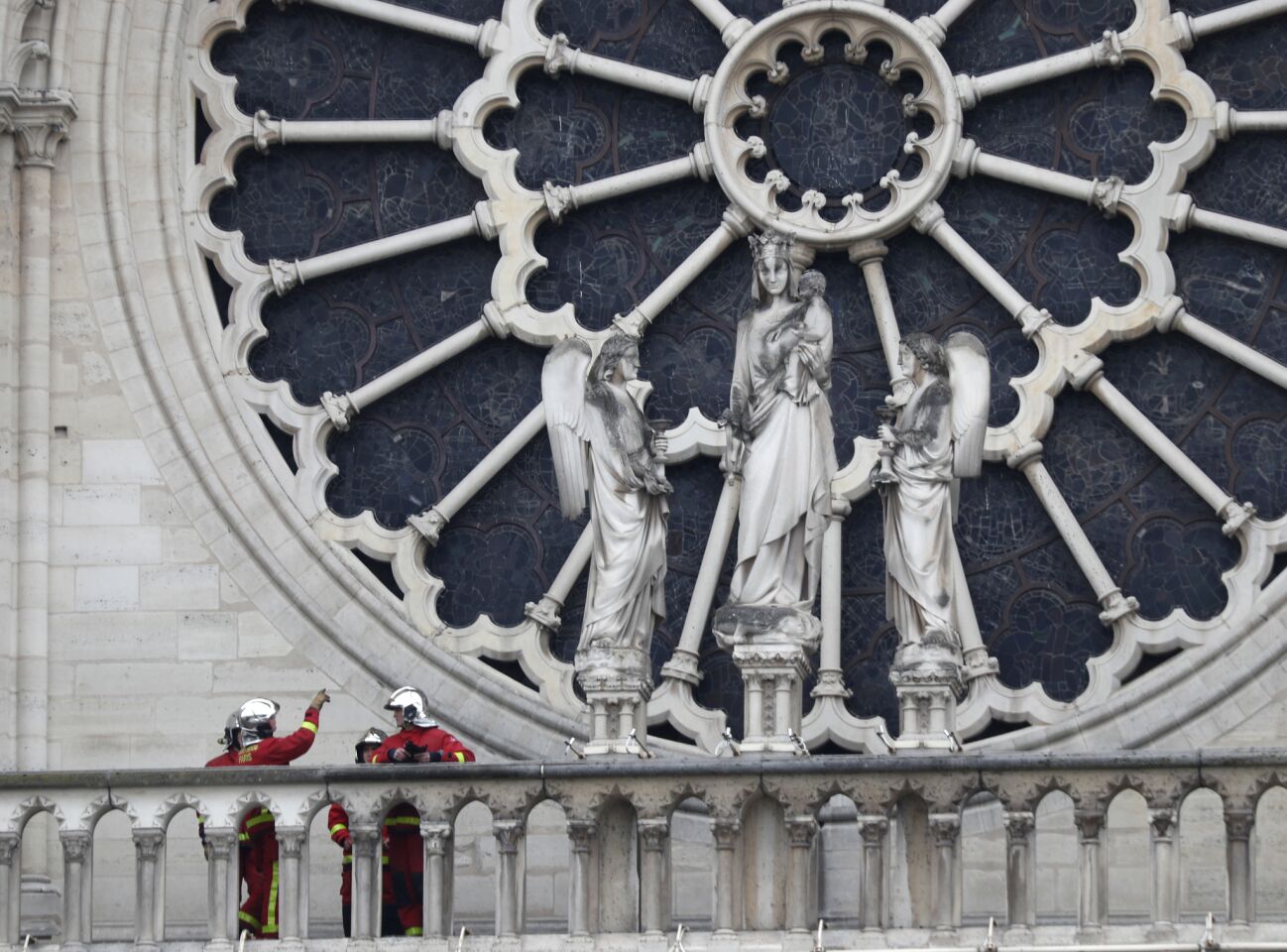 Firefighters talk near a rose window of Notre Dame Cathedral in Paris. Experts assessed the damage April 16 to establish next steps to save what remained the day after a devastating fire.