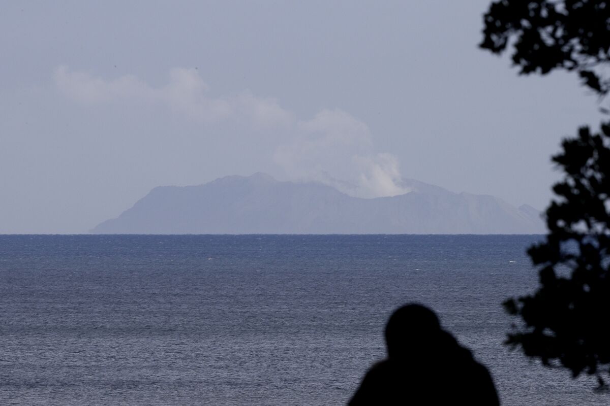 FILE - In this Dec. 10, 2019, file photo, a man watches as a plume of steam is seen above White Island early morning off the coast of Whakatane, New Zealand. A man who died in an Australian hospital had become the 20th casualty of the New Zealand volcano eruption more than a month ago, officials said on Monday, Jan. 13, 2020. (AP Photo/Mark Baker, File)