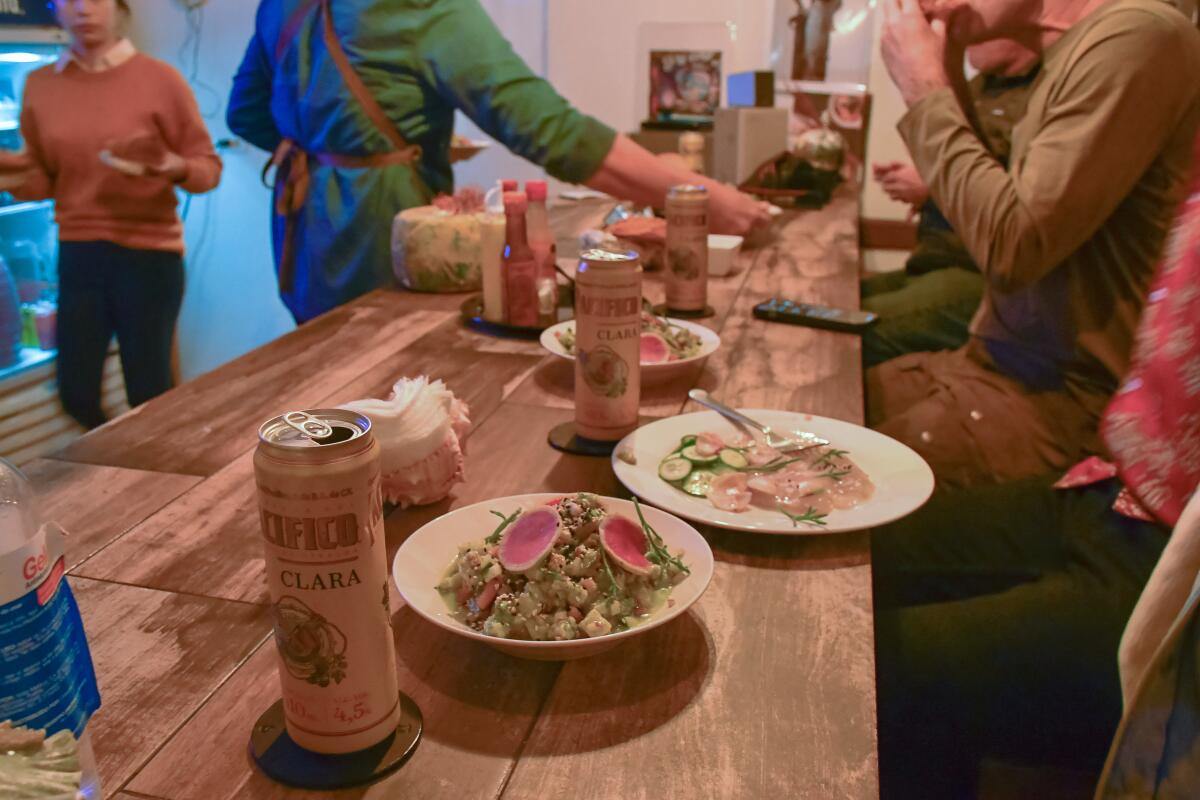 Canned drinks and plates of food on a long table surrounded by people