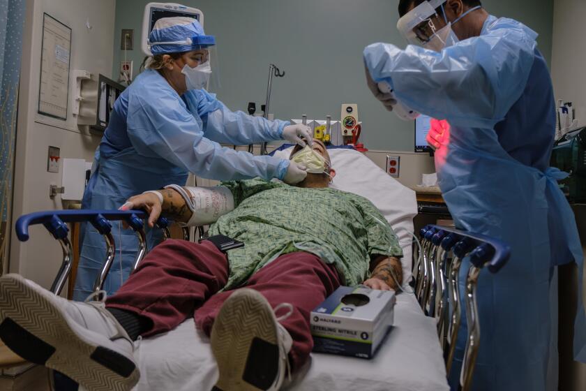 Registered nurses Shauna Stanfill, left, and Arnold Garcia administer care for Michael Weiss after he was admitted with possible COVID-19 symptoms at Sharp Chula Vista Medical Center on April 10, 2020.