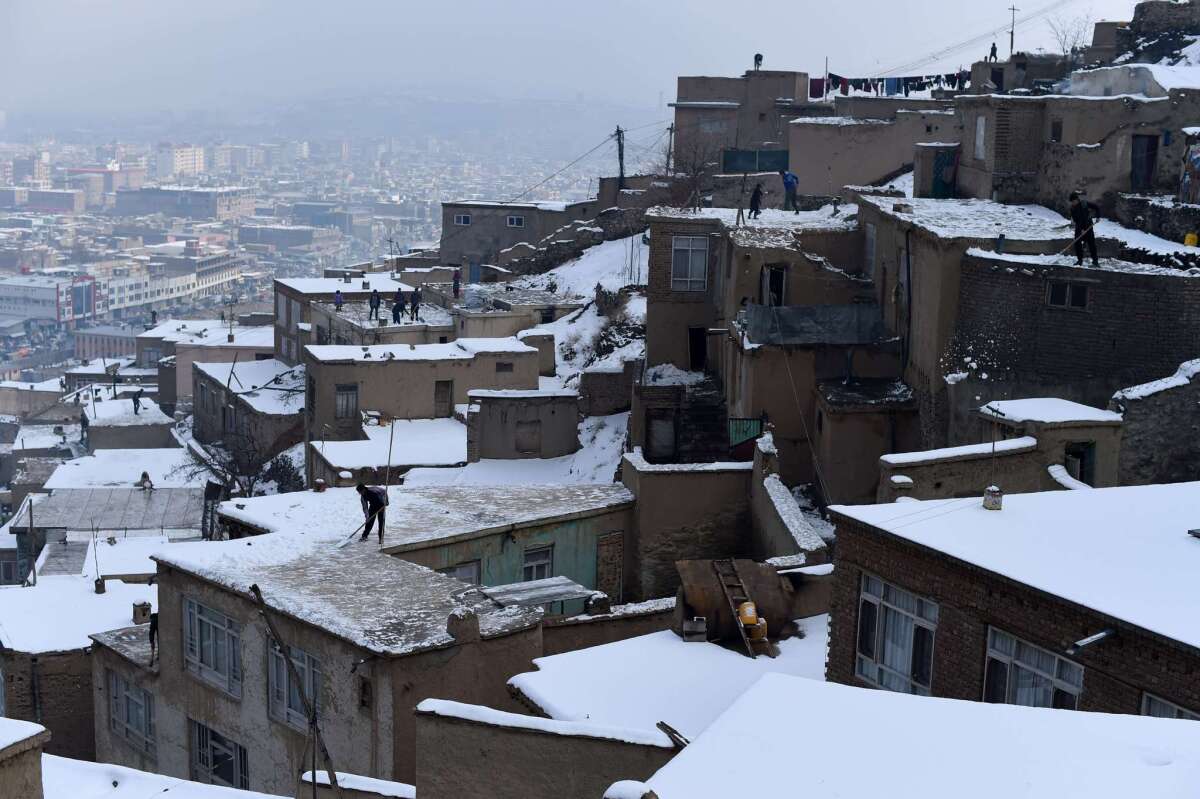 Afghan residents remove snow from the roofs of houses overlooking Kabul on Jan. 25. In the northeast of the country, at least 100 people have been killed in avalanches following severe snowfall.