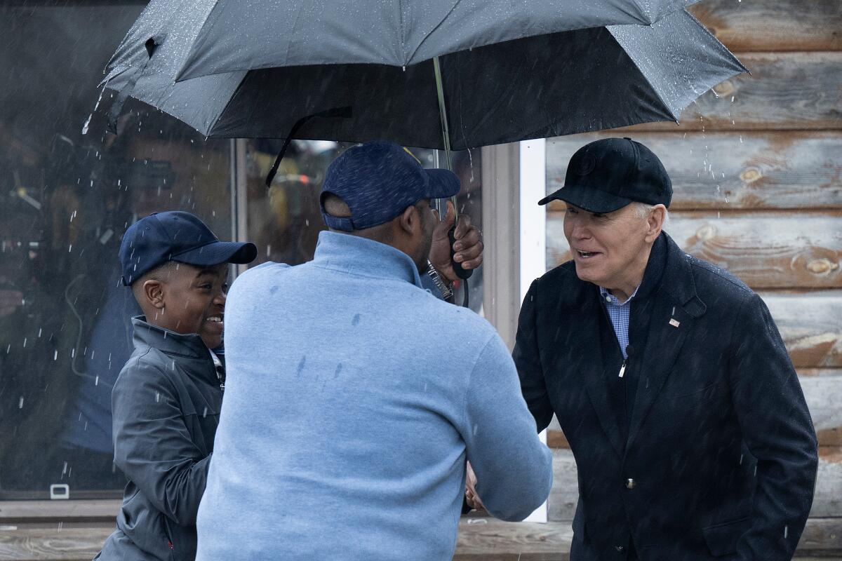 President Biden greeting a man and a teenager under umbrellas