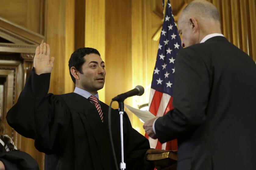 FILE - Mariano-Florentino Cuellar, left, is sworn in as an associate justice to the California Supreme Court by Gov. Jerry Brown during an inauguration ceremony in Sacramento, Calif., Monday, Jan. 5, 2015. The California Supreme Court ruled Thursday, March 25, 2021 that judges must consider suspects’ ability to pay when they set bail, essentially requiring that indigent defendants be freed unless they are deemed too dangerous to be released awaiting trial. Cuellar wrote on behalf of the court — conditions that “in many cases protect public and victim safety as well as assure the arrestee’s appearance at trial.” (AP Photo/Rich Pedroncelli, file)