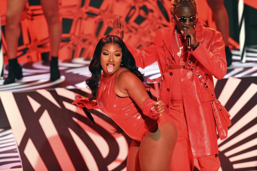 A woman dressed in a red latex body suit dancing and sticking her tongue out