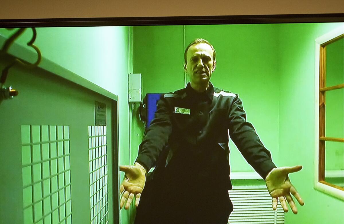 A man in dark clothes holds out his hands in a green room 