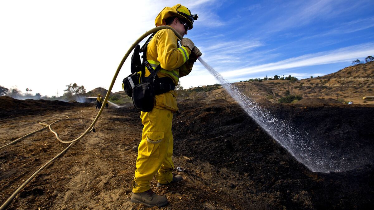 Aaron Wittmers of the Vacaville Fire Protection District douses a smoldering field of compost Saturday in Bonsall, Calif.