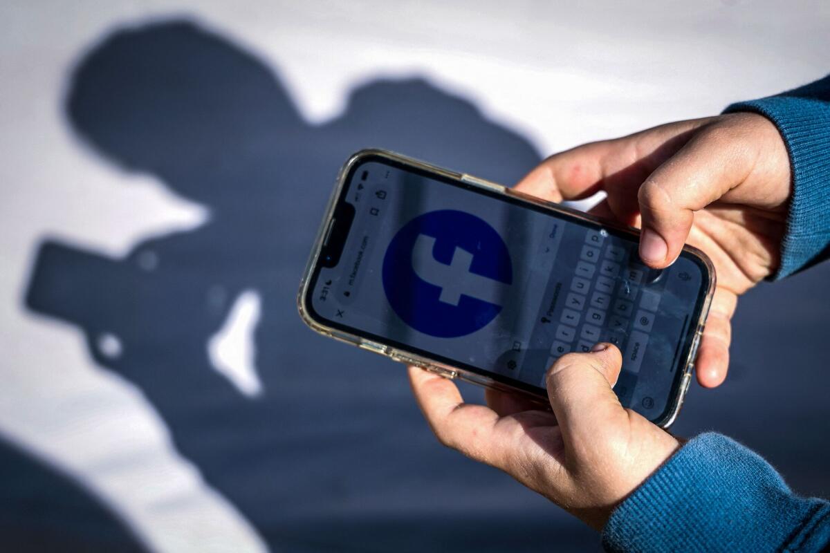Hands hold a cellphone with the Facebook logo on the screen