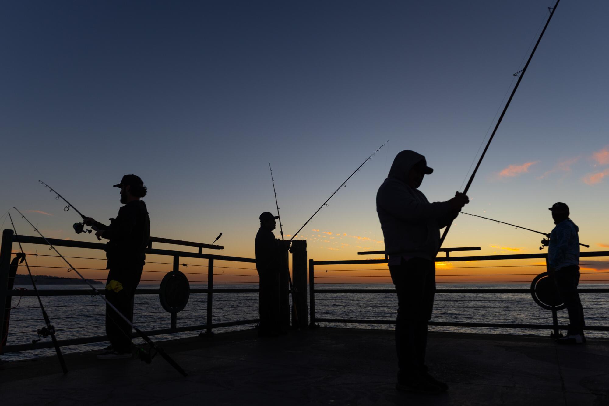 Fishermen stand on the end of a pier at sunset. 