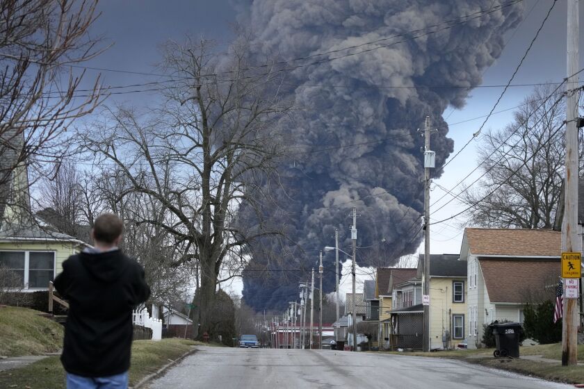 FILE - A man takes photos as a black plume rises over East Palestine, Ohio, as a result of a controlled detonation of a portion of the derailed Norfolk Southern train, Feb. 6, 2023. After toxic chemicals were released into the air from a wrecked train in Ohio, evacuated residents remain in the dark about what toxic substances are lingering in their vacated neighborhoods while they await approval to return home. (AP Photo/Gene J. Puskar, File)
