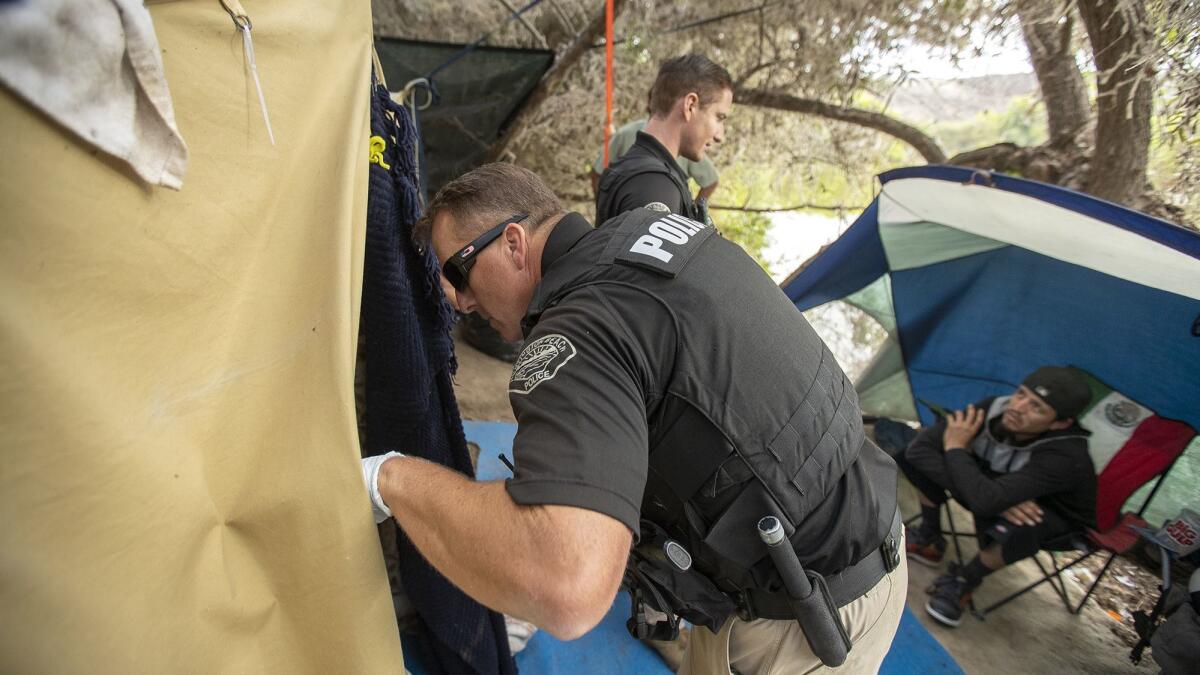Officer Gabe Ricci of the Huntington Beach Homeless Task Force looks in a tent while Officer Daniel Chichester talks with Rigoberto Espinosa, right, at a homeless encampment off Ellis Avenue on Wednesday.