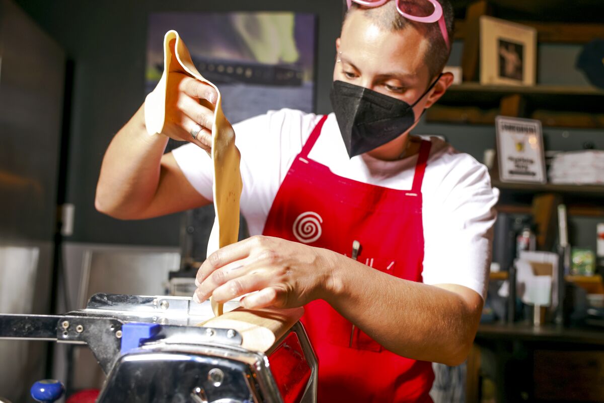 A man wearing a face mask runs dough through a pasta maker.