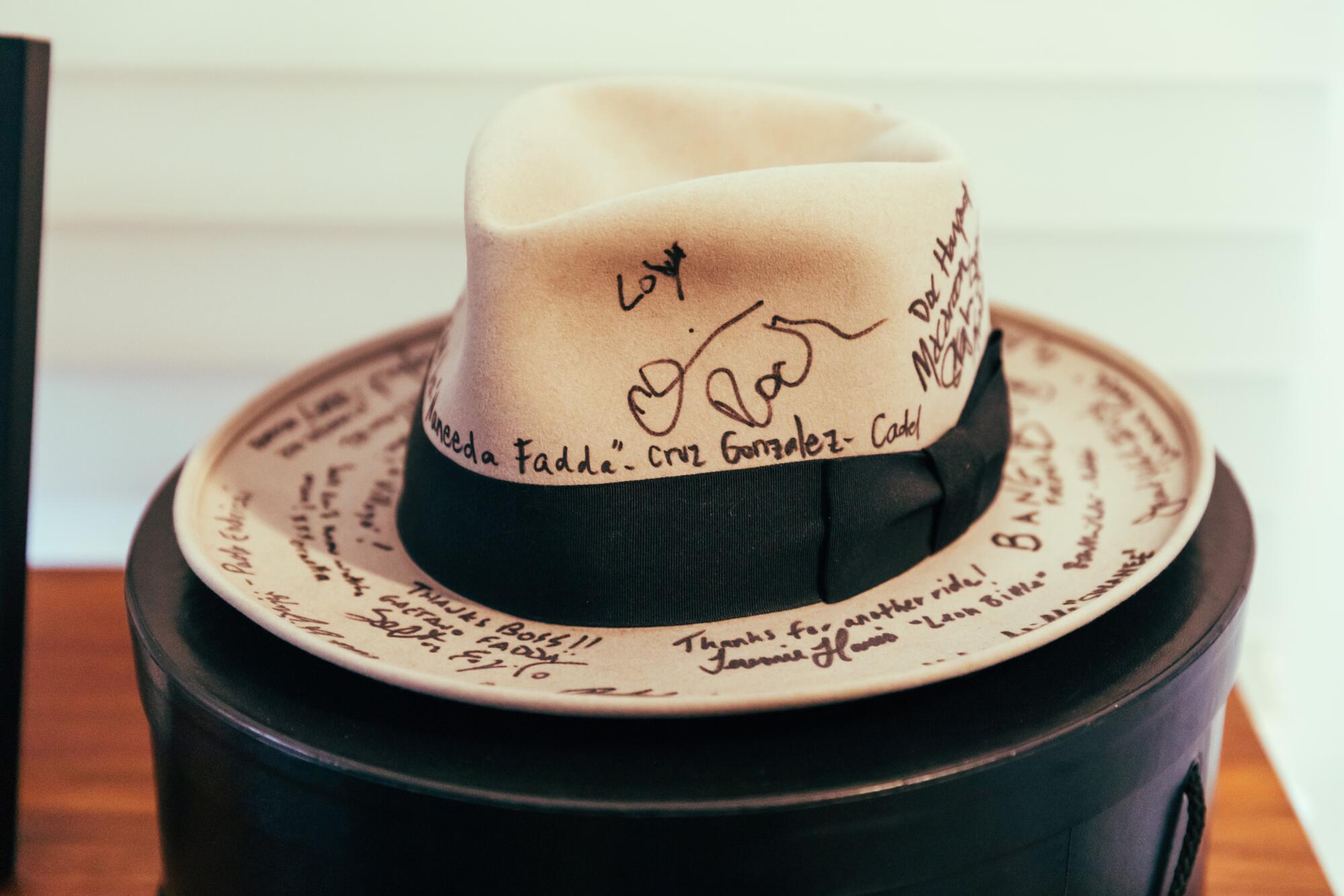 A tan straw hat with a black ribbon covered in signature.