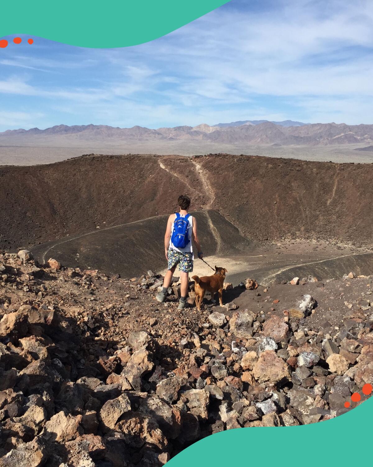 A man stands at the edge of a crater in the desert.