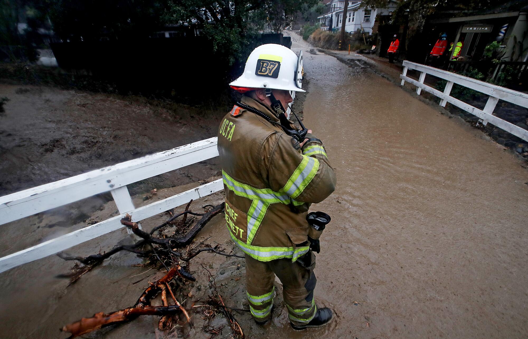 A fire official in protective gear watches muddy water flow past
