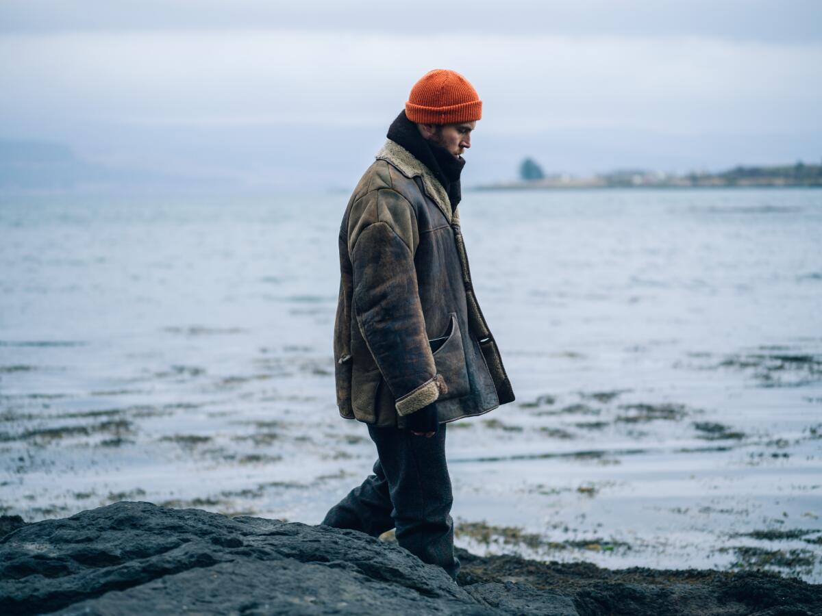 A man in a cap and coat walks along a shoreline in the movie "Shepherd."