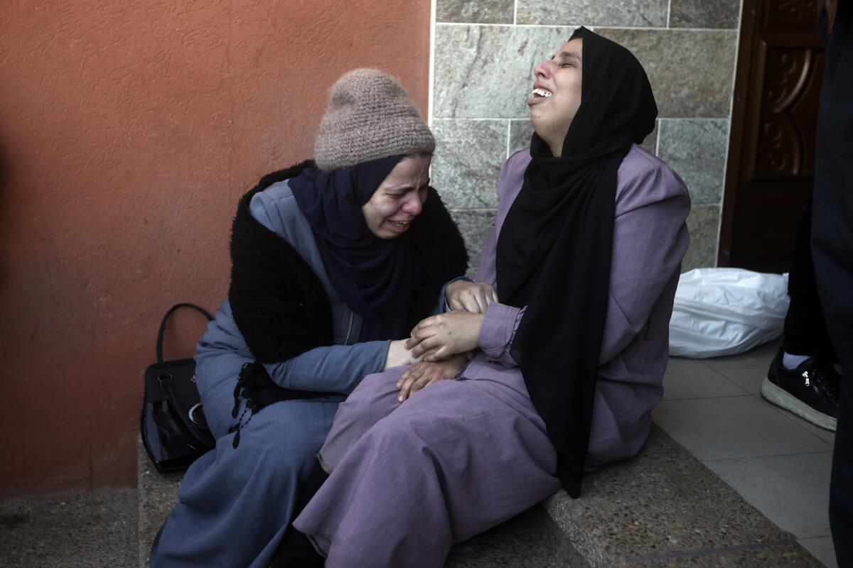 Two Palestinian women sit together weeping