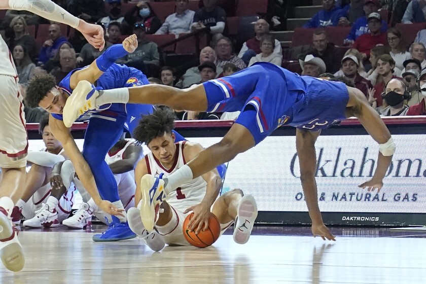 Kansas forward David McCormack, right, dives over Oklahoma forward Jalen Hill (1) in front of teammate forward Jalen Wilson, left, in the first half of an NCAA college basketball game Tuesday, Jan. 18, 2022, in Norman, Okla. (AP Photo/Sue Ogrocki)
