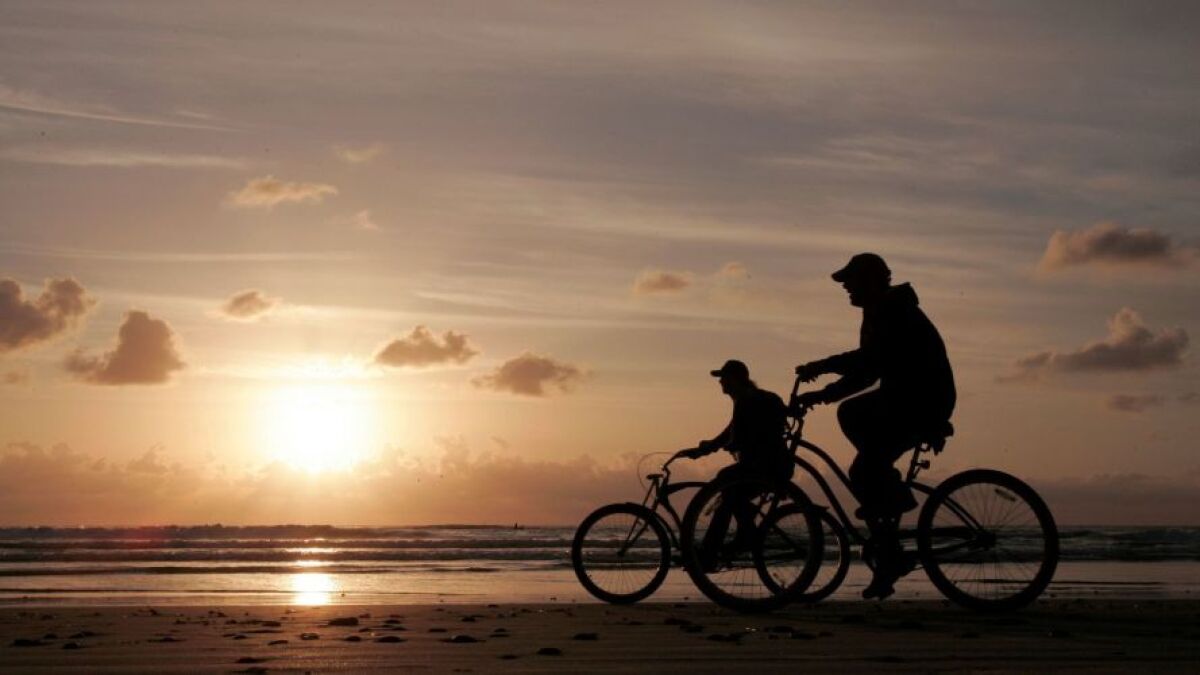 Two bicyclists ride along the water's edge at sunset at S. Cardiff State Beach along S. Coast Highway 101.