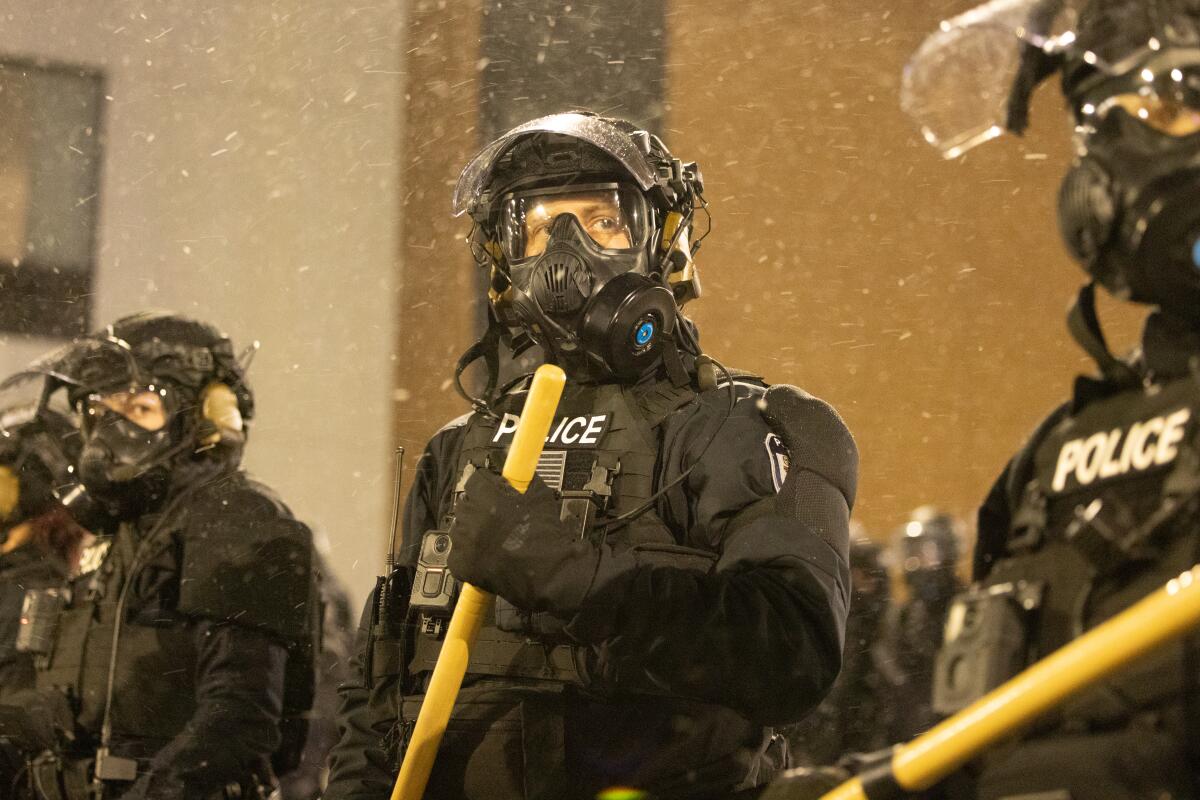 Officers in dark uniforms with tear-gas masks and face shields