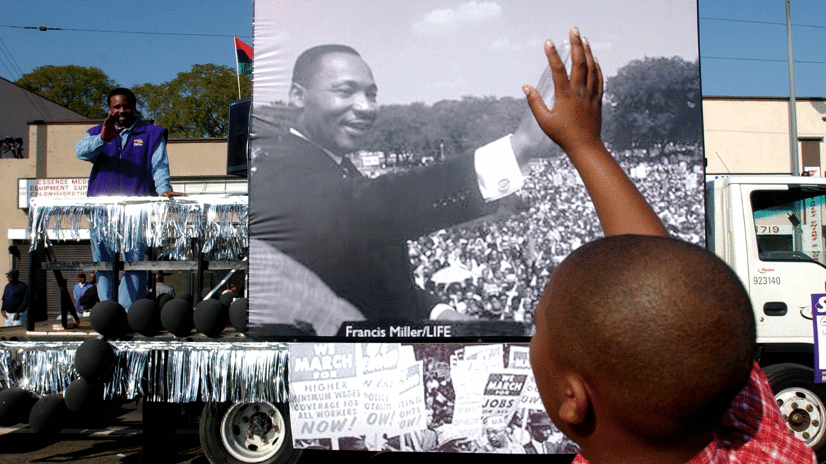 A young spectator seems to create a bridge with the past as his raised hand appears to connect with an image of Martin Luther King Jr. that rolls by during the parade along Martin Luther King Blvd. in Los Angeles.