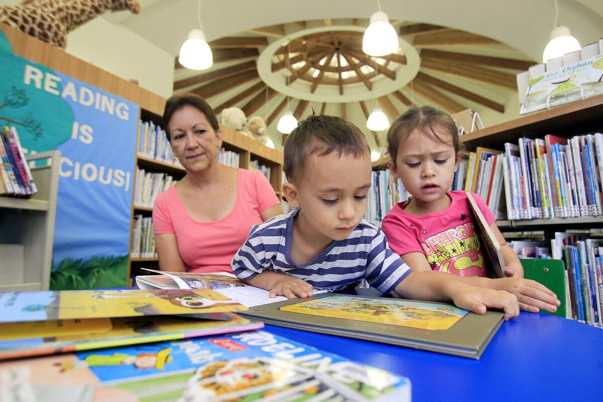 Catalina Ospina, left, watches as three-year-old twins Jeremiah, center, and Melia Kearns look through children's animal books during the reopening of Donald Dungan Library in Costa Mesa on Wednesday.