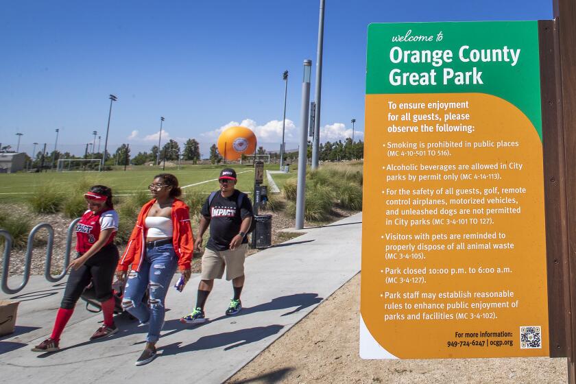 Irvine, CA - July 28: A softball player and family walk past a sign at the Great Park on Wednesday, July 28, 2021 in Irvine, CA. The Irvine City Council considered three names for the site at a meeting Tuesday: the Irvine Great Park, the Great Park of Irvine and the Great Park. Ultimately, the council voted 4 to 1 to change the name to the Great Park - a nickname many Orange County residents already use to identify the swath of land that was formerly the El Toro Marine Corps Air Station. (Allen J. Schaben / Los Angeles Times)