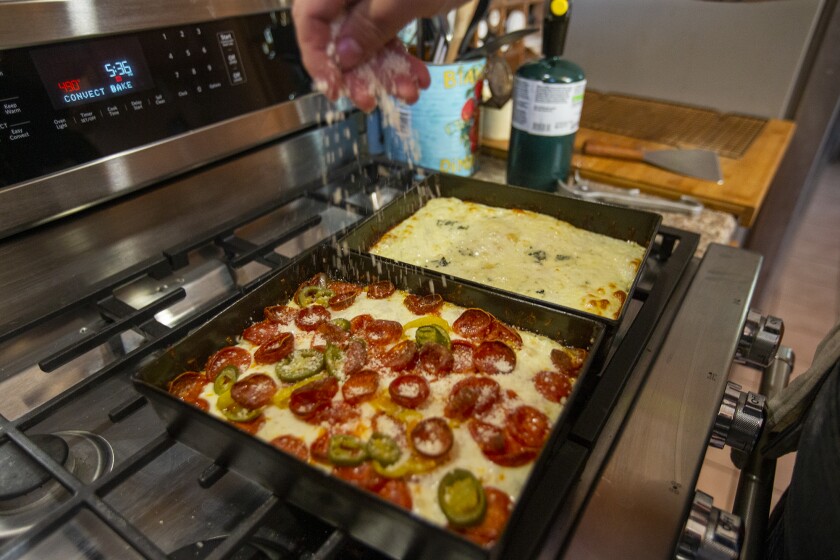 Derek Bracho sprinkles cheese onto some homemade focaccia-bread pizza at his home in Anaheim.