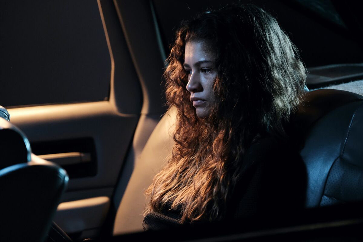 A young woman sits in the back seat of a car at night, lost in thought