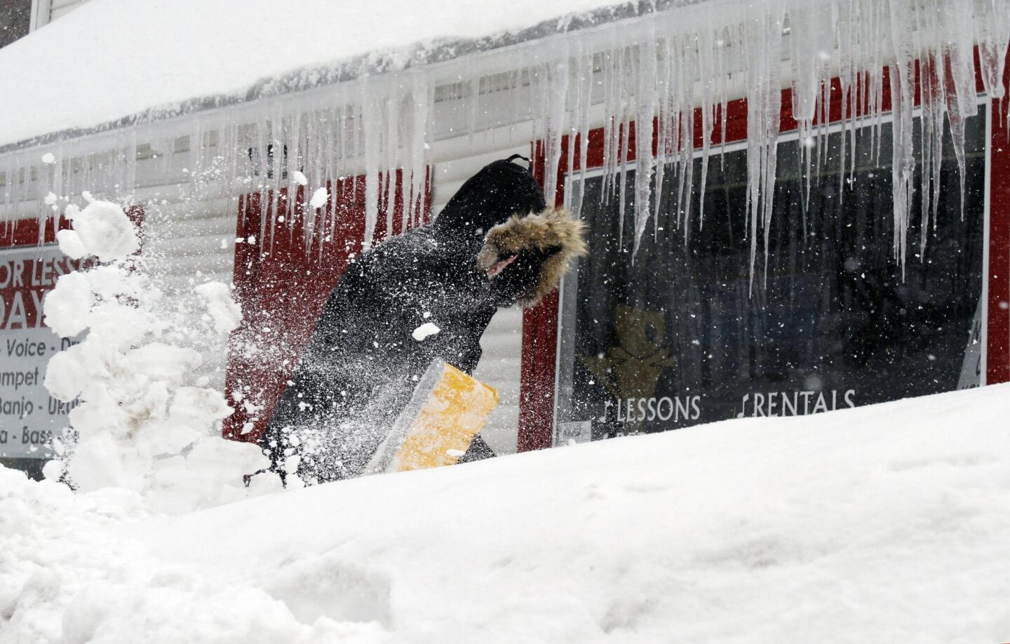 Corbit Larson clears snow in front of icicles hanging from his Centre Music store in Framingham, Mass., on Monday.